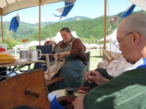 two people sitting in the shade of a pavilion creating historical objects using historical handcrafting techniques